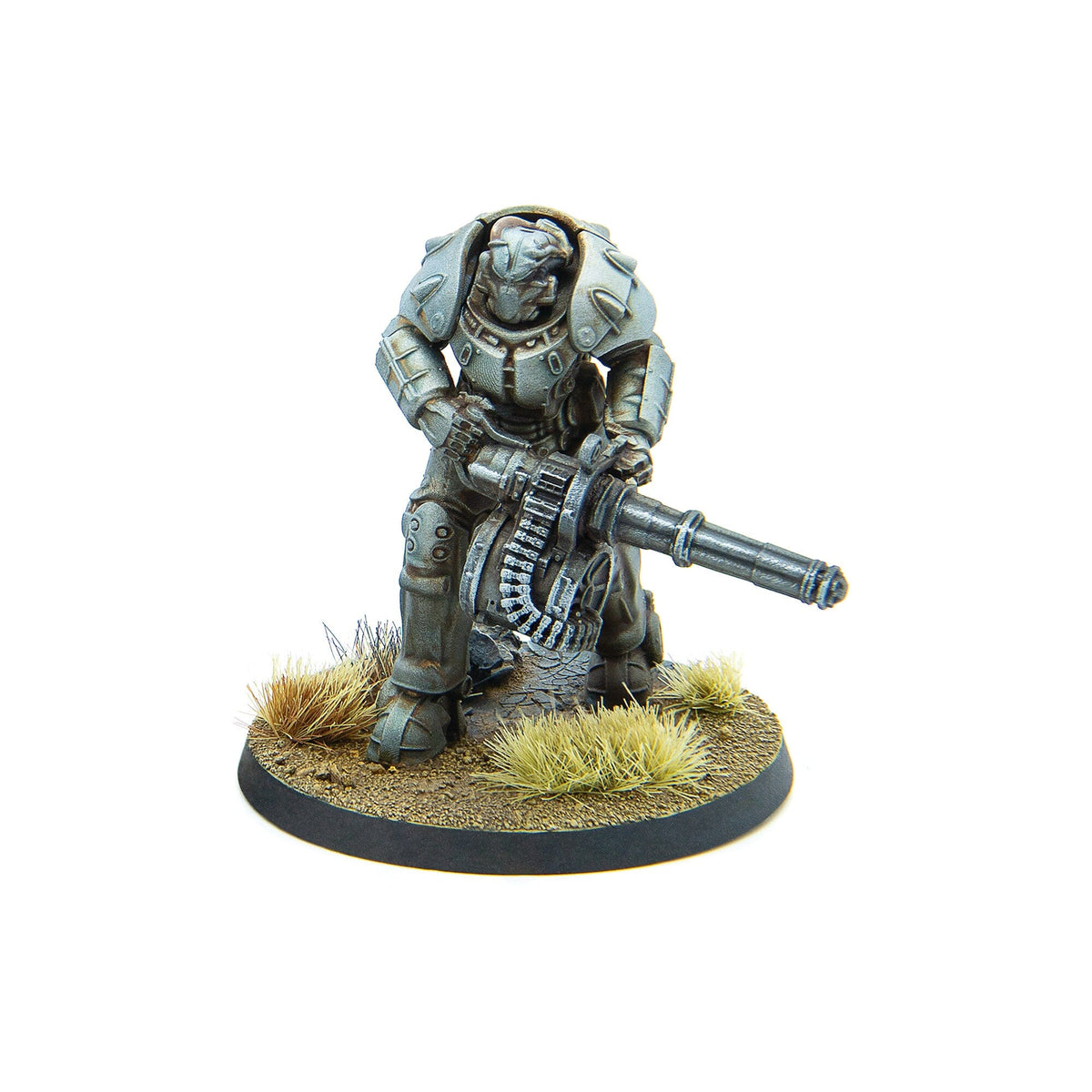 A silver armored miniature soldier operates a heavy belt-fed machine gun, standing on a textured, grassy base