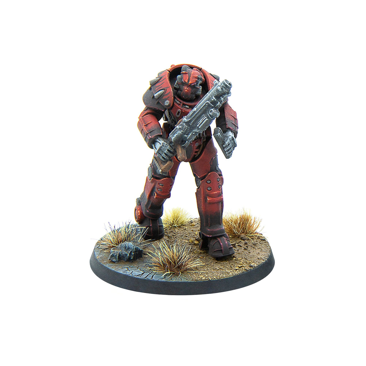 A red armored miniature sci-fi warrior with a rifle, standing on a cracked earth base with dry grass