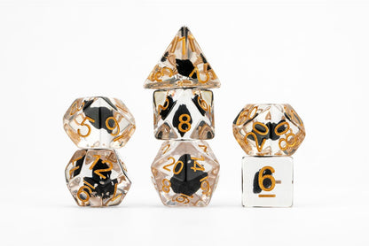 Clear polyhedral RPG dice set with black inclusions and gold numbers, stacked on a white background