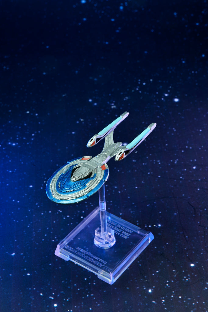 A silver Star Trek starship model with blue accents, displayed on a clear stand against a dark blue starry background