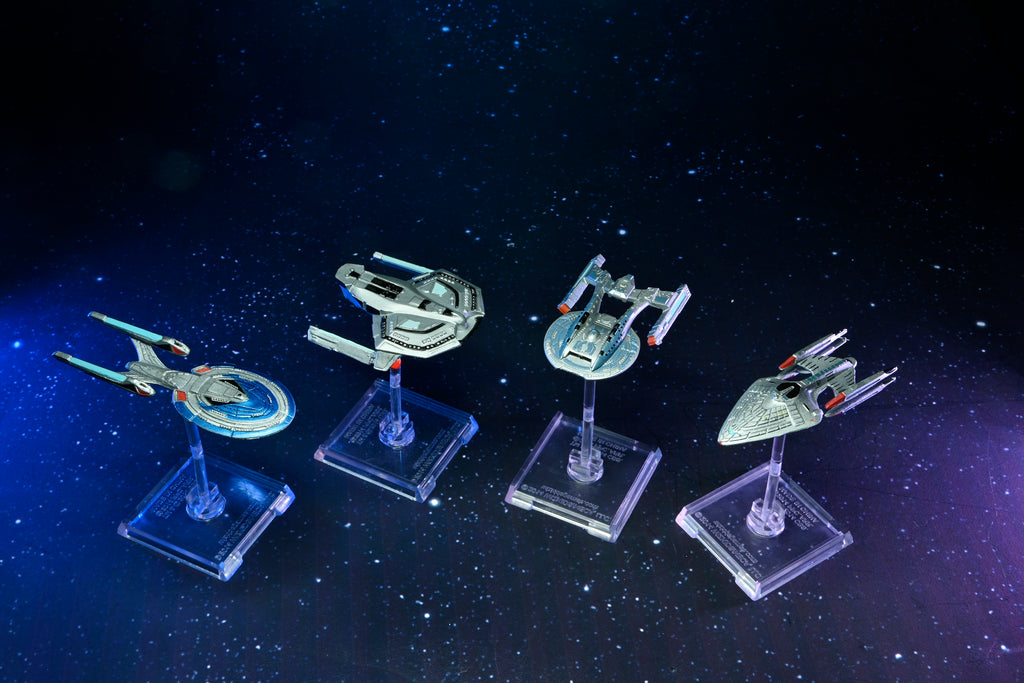 Four miniature Star Trek ships displayed on clear stands against a starry, dark blue space background