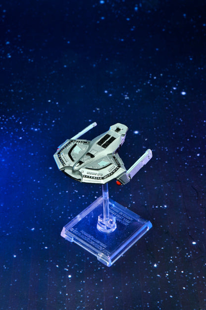A miniature Starfleet Defiant-class spaceship model on a clear stand, against a dark blue starry background
