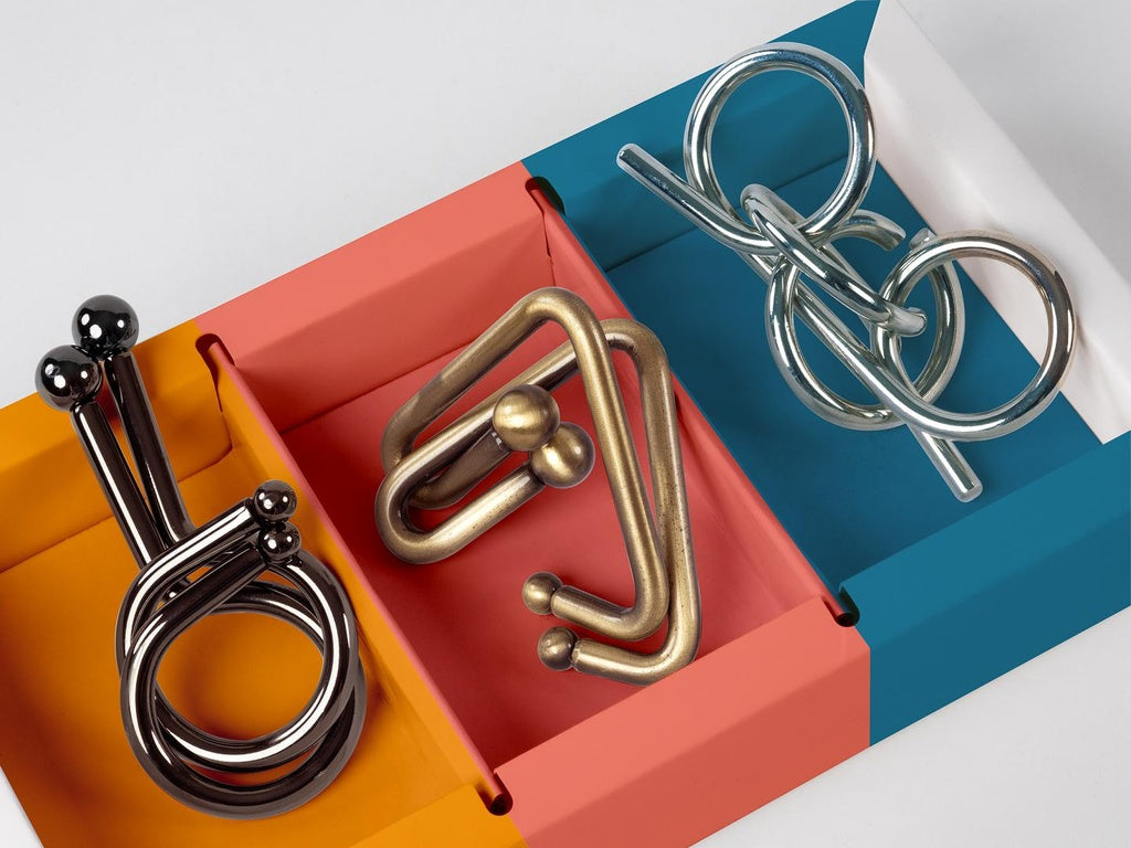Three intertwined metal wire disentanglement puzzles displayed in a colorful, segmented tray