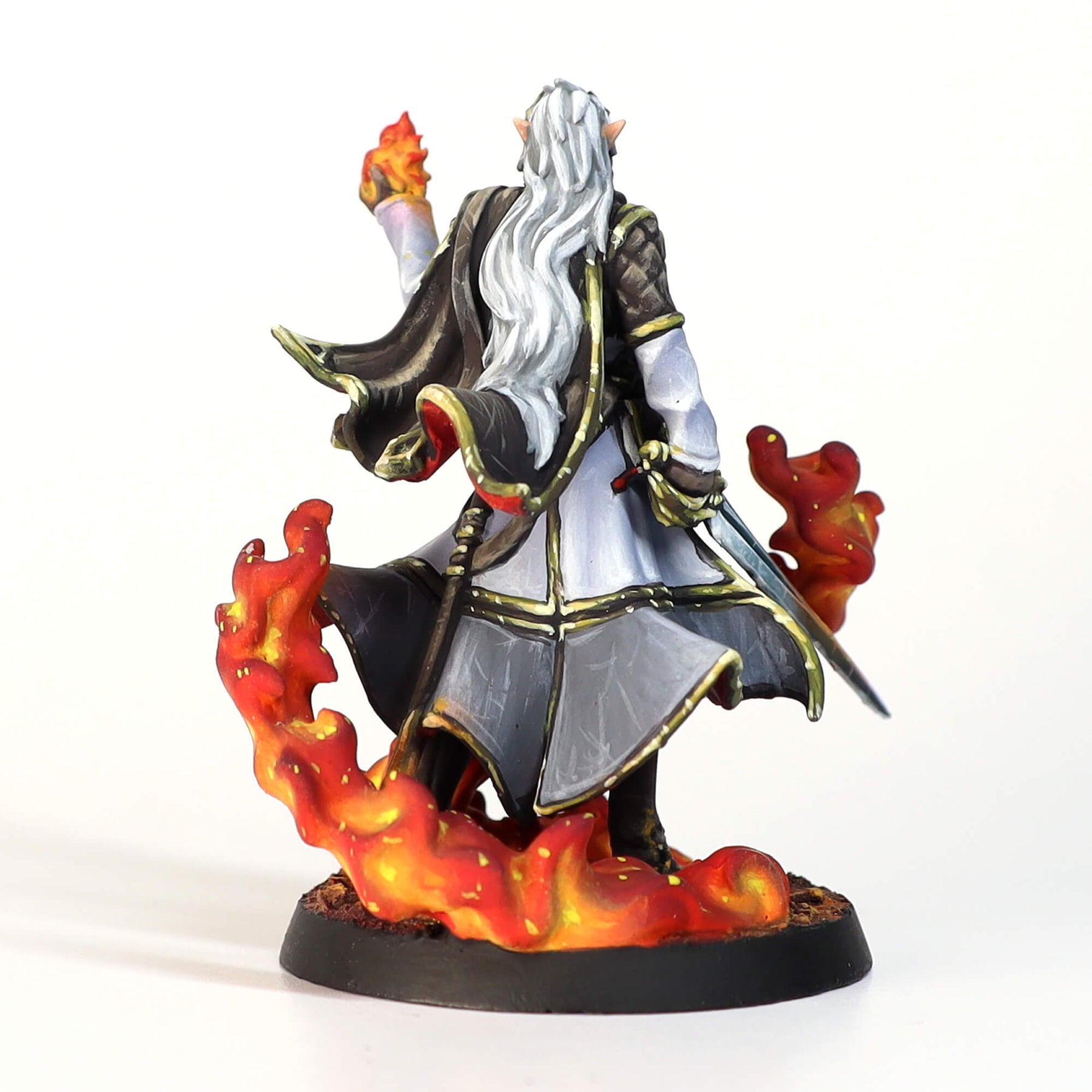 White-haired elf miniature in a dark cloak, seen from behind, holding a flaming hand and surrounded by fire at its base.