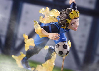 Anime figure of a soccer player in a blue uniform and yellow hair kicking a ball