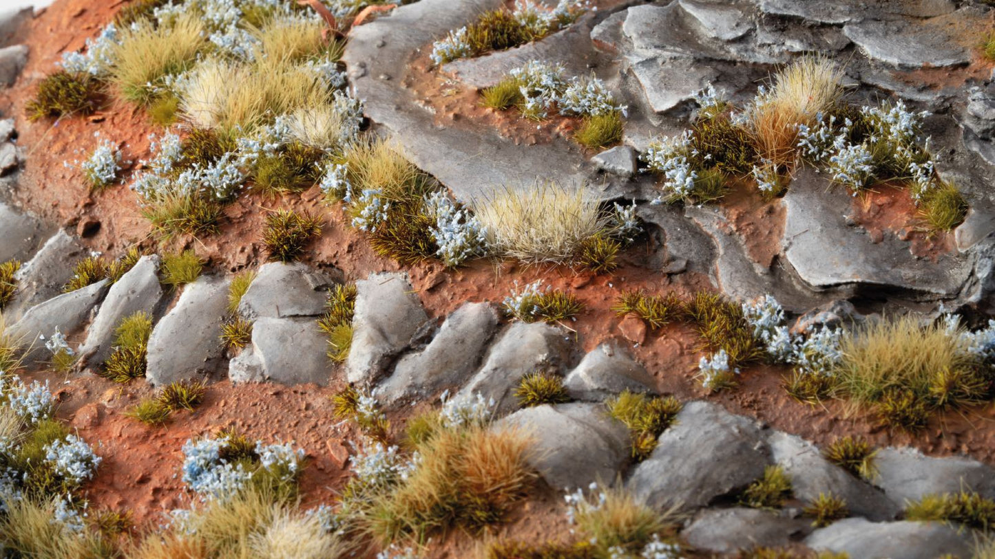 Miniature rocky desert landscape with red earth, layered gray stones, dry grasses, and white scatter