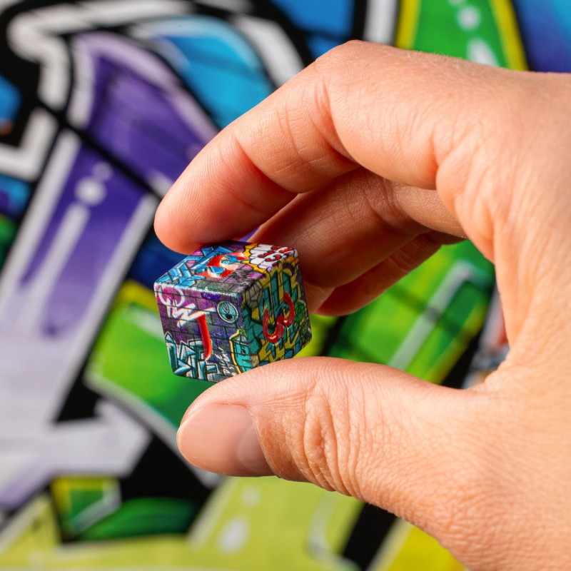 Hand holding a small graffiti-decorated cube against a blurred graffiti background