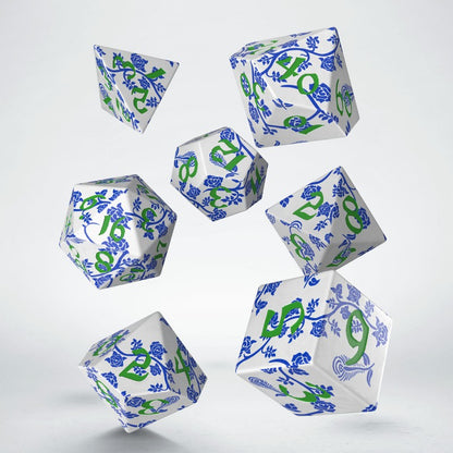 A set of seven white polyhedral dice with blue floral patterns and green numbers floating on a white background