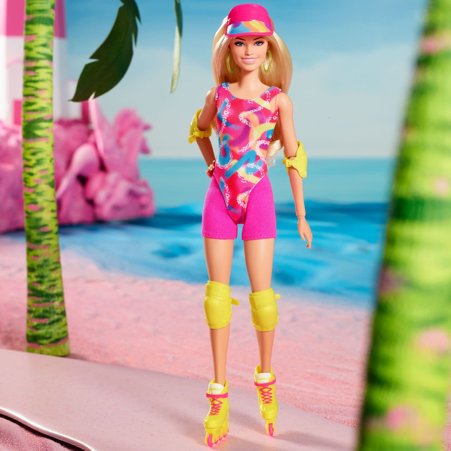 Barbie doll in a colourful leotard, pink visor, yellow pads, and roller skates, standing on a pink beach