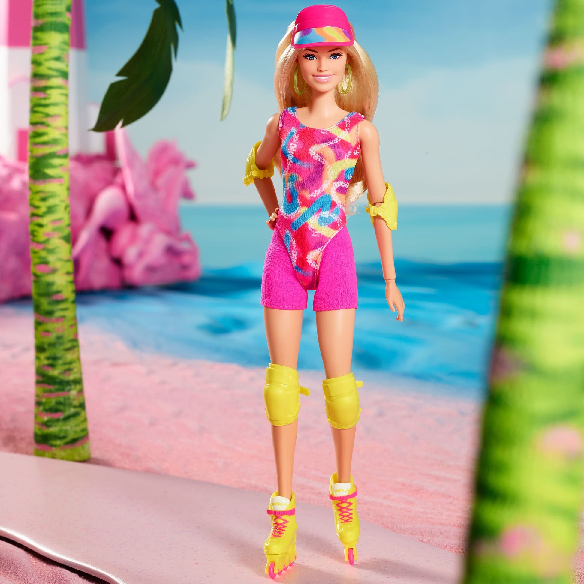 Barbie doll in a colourful leotard, pink visor, yellow pads, and roller skates, standing on a pink beach
