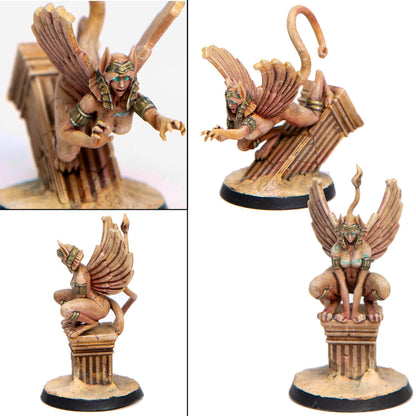 A tan winged female sphinx miniature with gold accents and teal eyes, crouching on a broken desert column