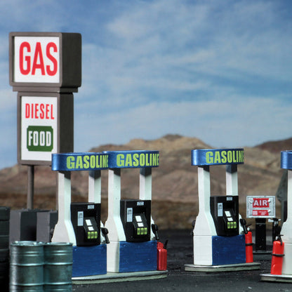 A model gas station with several blue and white pumps and a large sign for GAS, DIESEL, and FOOD, against a desert landscape