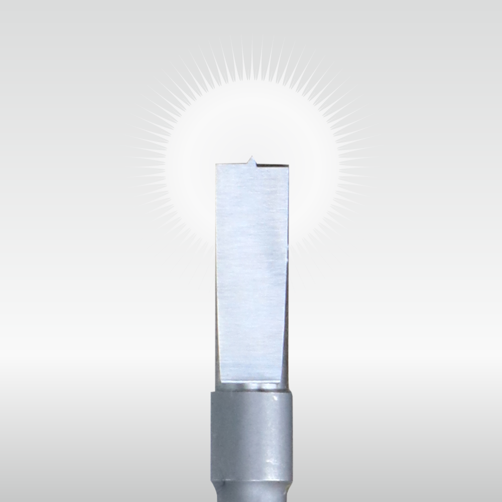 A silver metal tool bit with a notched rectangular blade and a bright sunburst behind it