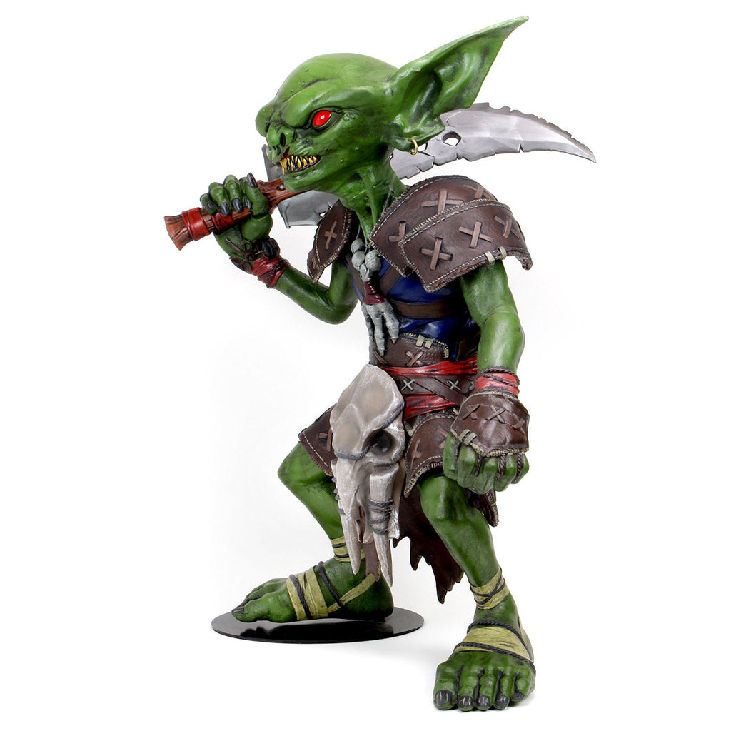 A green goblin statue with red eyes, sharp teeth, wearing primitive armor, holding a jagged sword over its right shoulder