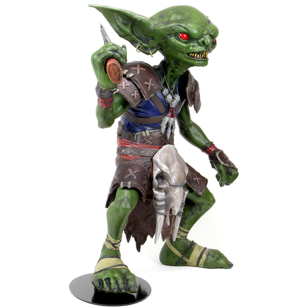 Green goblin figure with glowing red eyes, sharp teeth, and tribal armor, holding a dagger in its raised hand