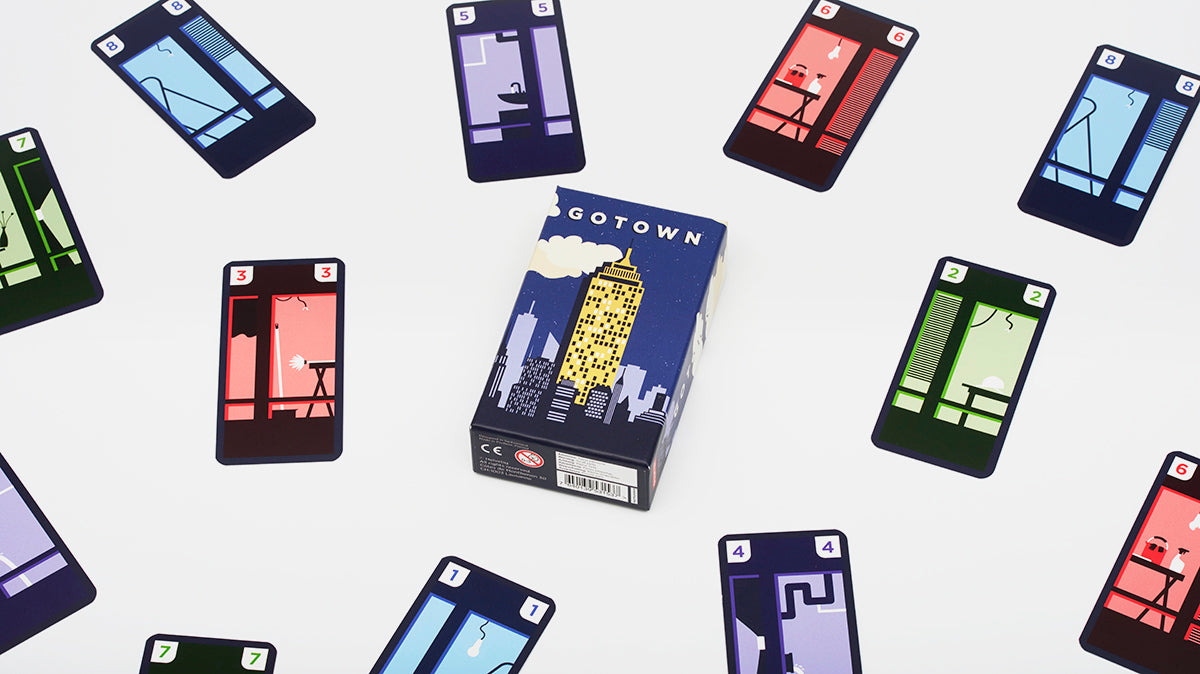 A deck of Gotown game cards and box centered among scattered individual cards featuring stylized apartment rooms at night