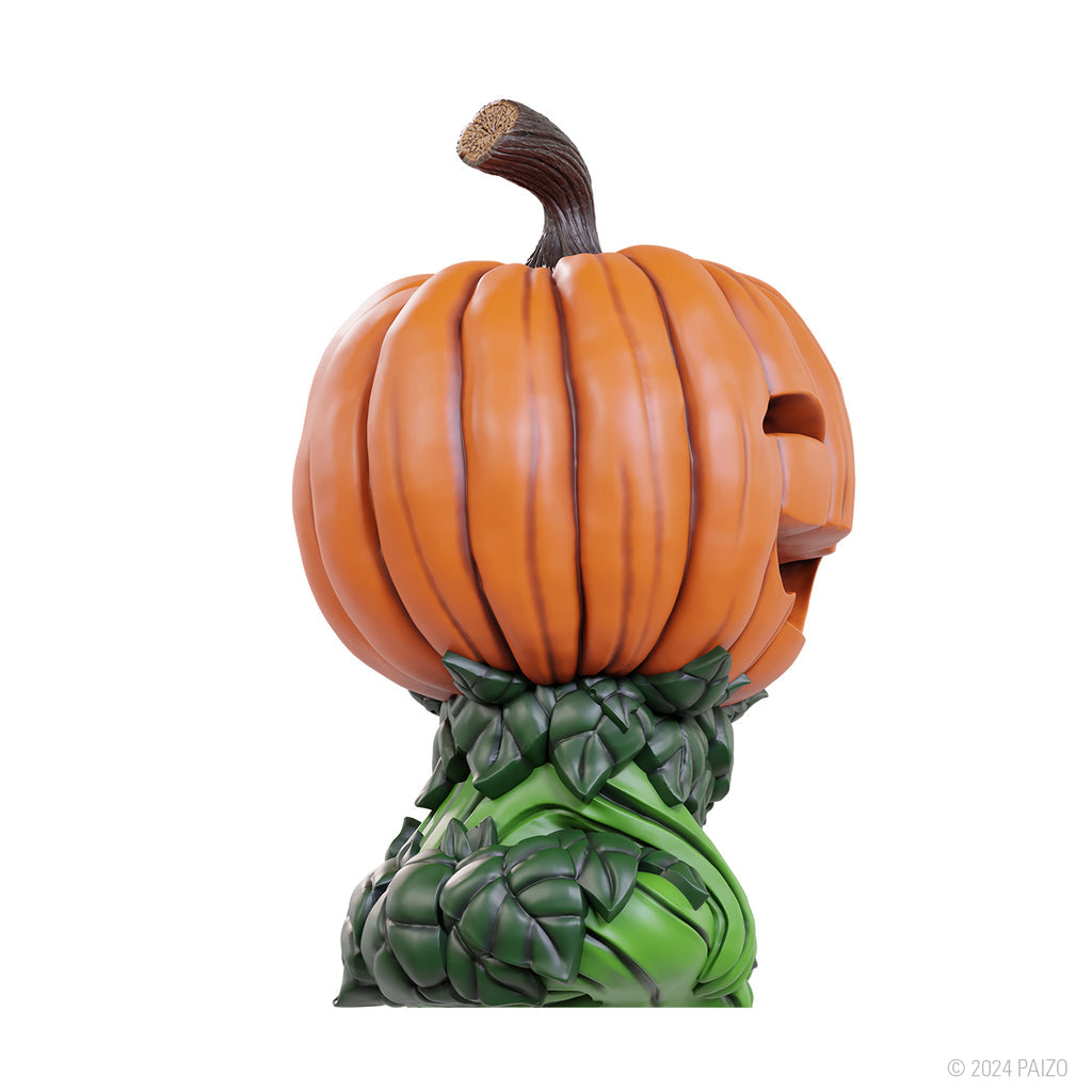 An orange gourd leshy figure with a carved face and brown stem, resting on a base of green leaves
