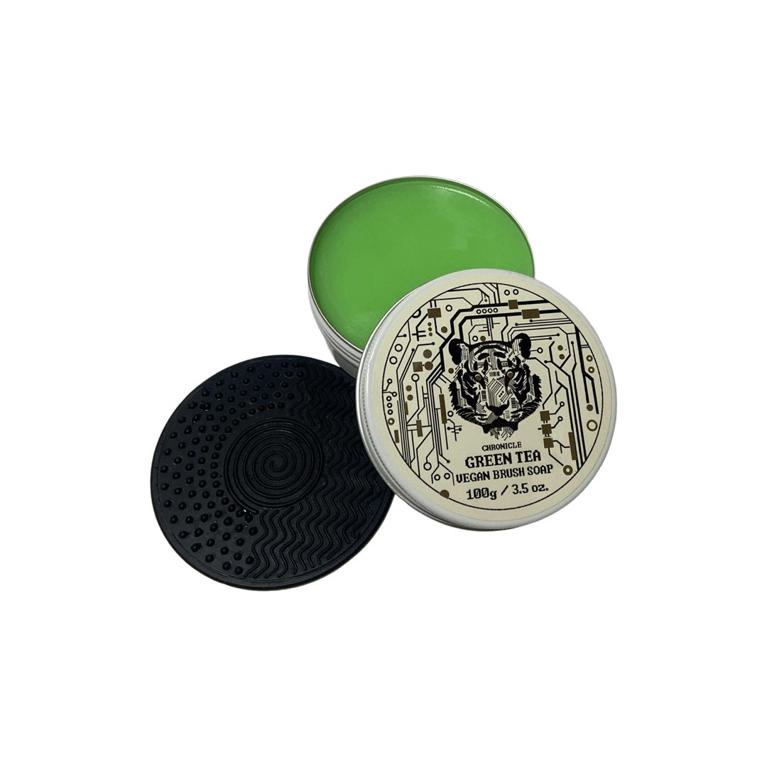 Open tin of green tea vegan brush soap with a tiger-designed lid, next to a black textured silicone cleaning mat