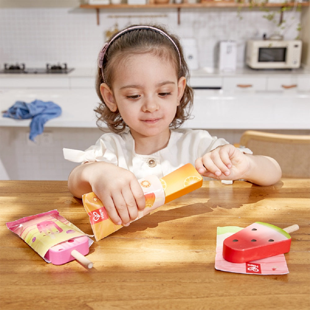 Young girl playing with colorful wooden popsicle play food on a table in a kitchen setting