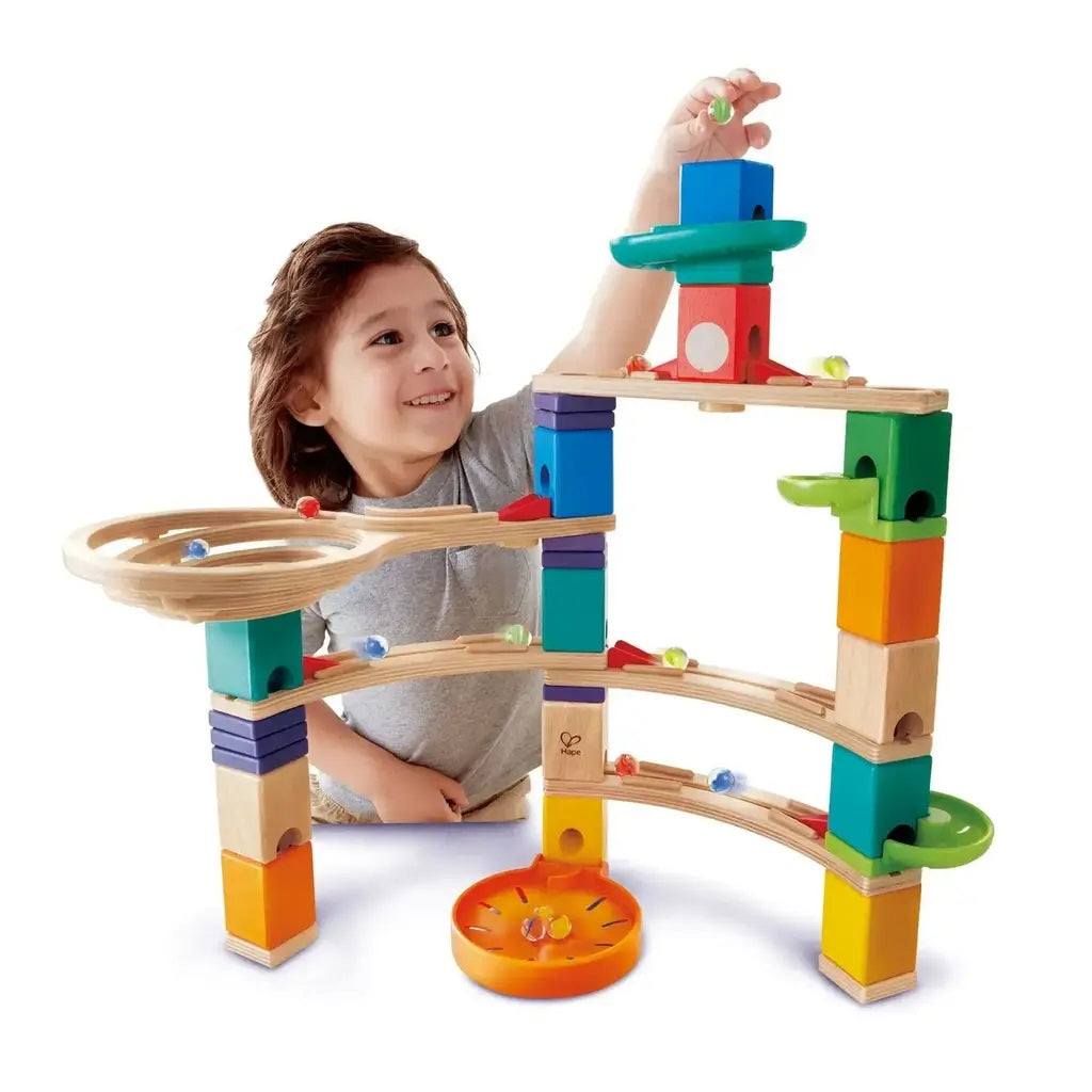 Smiling child dropping a marble into a large, colorful wooden marble run toy
