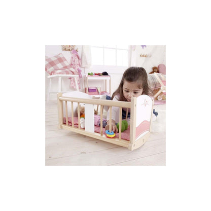 A young girl plays with a colorful stacking ring inside a wooden doll's crib, which also holds a doll.