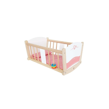 A light wood doll's rocking cradle with white ends, pink bedding with a heart design, and a small colorful stacking toy.