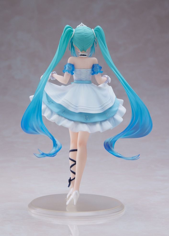 Back view of Hatsune Miku figure in a short, layered blue and white dress, tiara, and flowing teal pigtails on a display stand