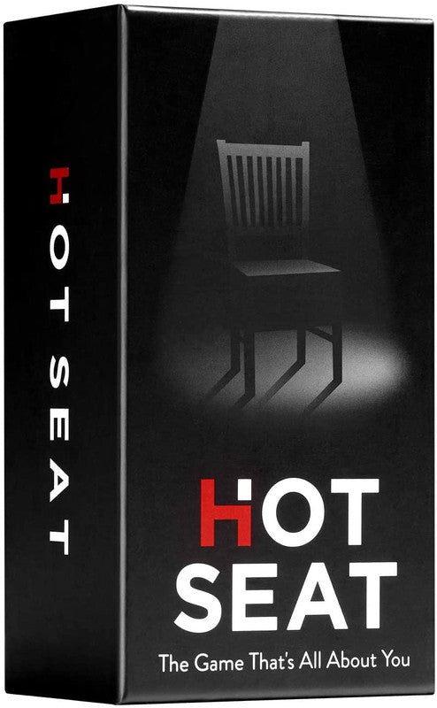 Black card game box with HOT SEAT in white text the H in HOT is red The Game That&#39;s All About You below the title chair visible in spotlight