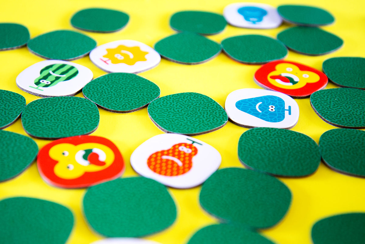 Colourful game tokens scattered on yellow features green textured pieces and white pieces with cartoon fruit animals and objects