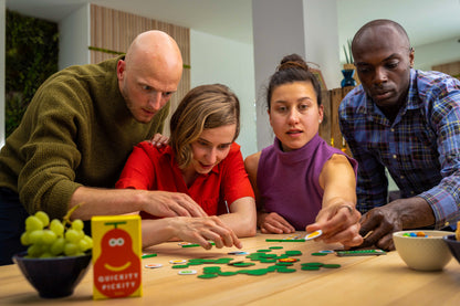 Four people intently playing a Quickity Pickity board game at a wooden table