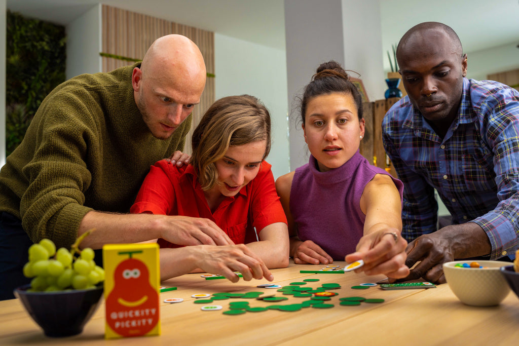 Four people intently playing a Quickity Pickity board game at a wooden table