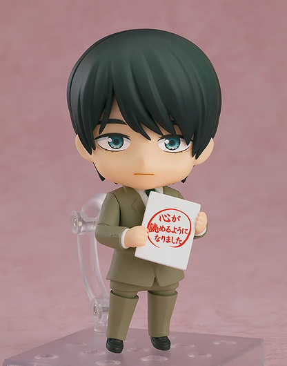 Figure of a man with dark green hair blue eyes and a tan suit holding a white sign with red Japanese text