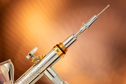 A detailed close-up of a shiny silver and gold "Infinity CR plus" airbrush, angled for precision painting