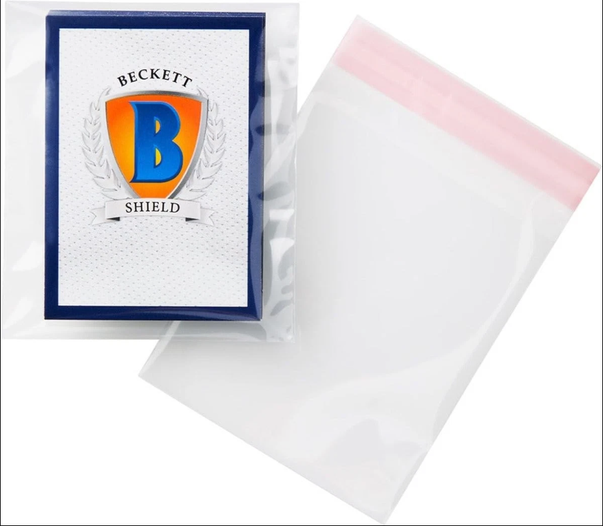 A Beckett Shield card holder in a clear sleeve, beside an empty clear plastic bag with a pink top seal