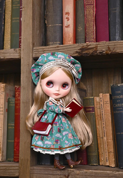 Good Smile Company Blythe Kendra the Bibliophile figure standing on a bookshelf, holding a book, wearing a green dress with book pattern and bonnet