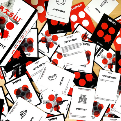 Batsu! game box and many cards scattered on a surface. Cards are black/white with red splatters, text, and silhouettes