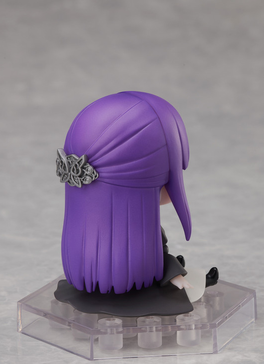 Figure of a young girl with long purple hair wearing a black dress and seated on a clear display base