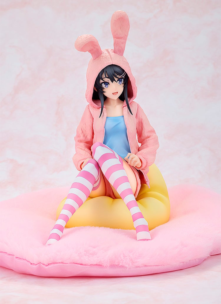 Anime figure in a pink bunny hoodie and striped socks, sitting on a yellow beanbag on a pink fluffy mat