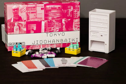 The Tokyo Jidohanbaiki board game box, miniature vending machine, tiny bottles in crates, assorted game pieces, and colourful cards are laid out on a dark table