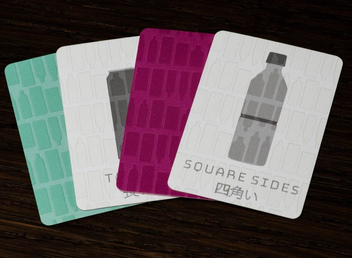 Four fanned cards on a wooden surface show patterns of various bottle shapes in teal, white, and magenta, with the front card displaying a grey bottle and SQUARE SIDES text