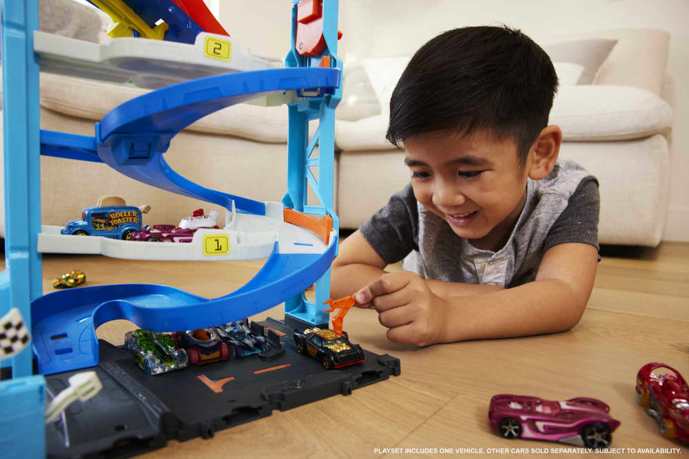 Smiling boy playing on the floor with a blue toy car track, placing a black car into the playset