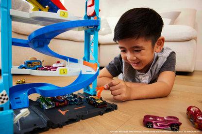 Smiling boy playing on the floor with a blue toy car track, placing a black car into the playset