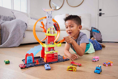 Excited boy plays with Hot Wheels track set, launching a car on its loop; toy cars on the floor