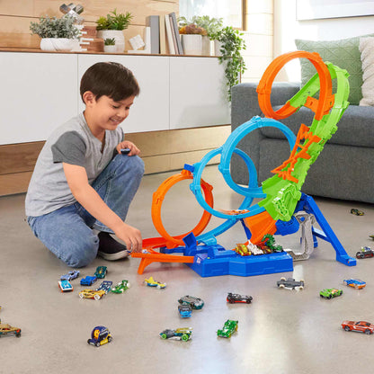 Smiling boy launching a toy car on a colorful Hot Wheels track with multiple loops and many cars on the floor