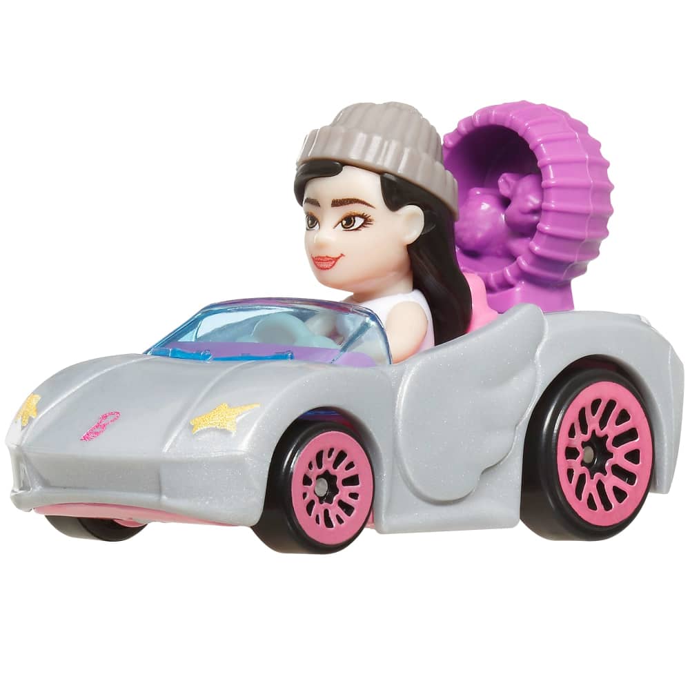 A smiling toy doll in a grey beanie sits in a sparkling gray convertible with pink wheels and a large purple coiled accessory