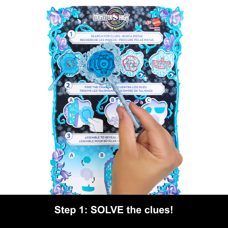 Hand uses a blue wand on a Monster High Ultimate Secret Mysteries game board, revealing clues on heart and skull shapes, blue and purple floral border. "Solve the clues!"