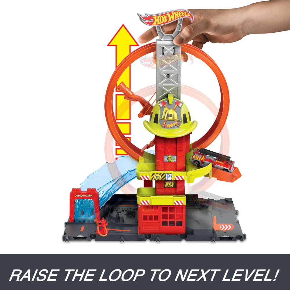 A hand raises a Hot Wheels fire station playset's orange loop, with a fire truck, helmet, and water spray