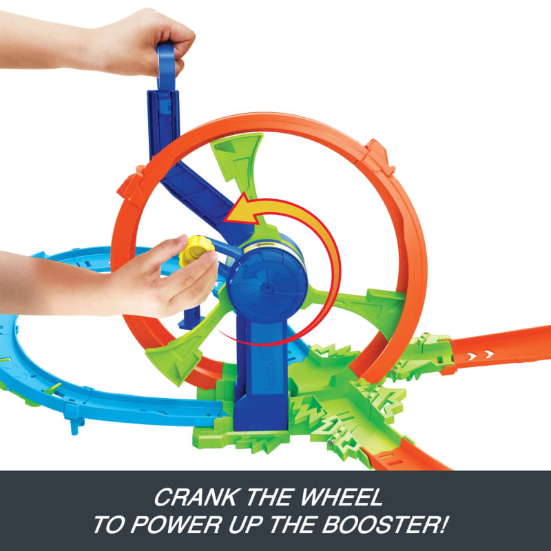 Child's hands cranking a yellow knob on a multi-colored toy car track booster with a large orange loop and green ramps