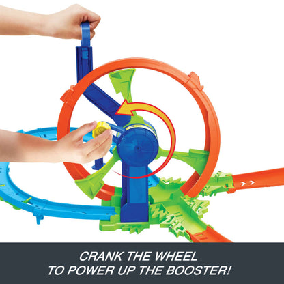 Child's hands cranking a yellow knob on a multi-colored toy car track booster with a large orange loop and green ramps