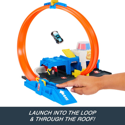 A hand launches a toy car through an orange track loop over a blue and white police station playset